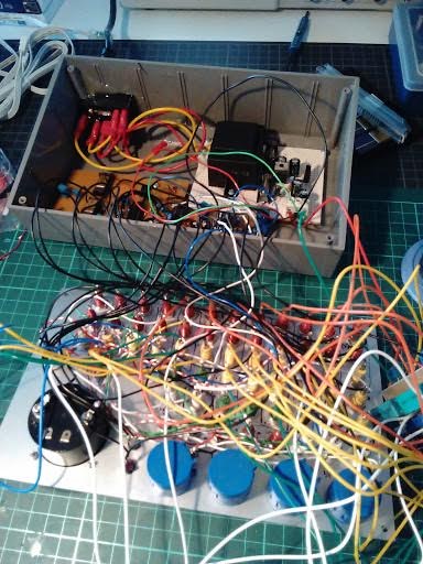 The 2017 replication with its case open: a transformer on a white circuit board at upper left, a brown measuring card, a dense tangle of coloured wires, and three blue capacitors visible at the lower right.